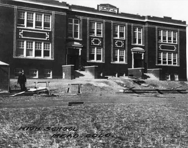 view of the Mead Consolidated school while still under construction. There is a man standing in front of the building and building materials are scattered about.