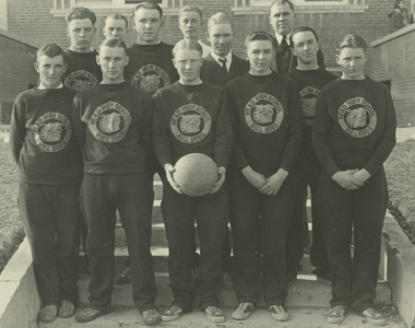 The 1930-1931 Mead school boys basketball team. Eleven boys and their coach are standing. The center front boy is holding the basketball down by his waist.